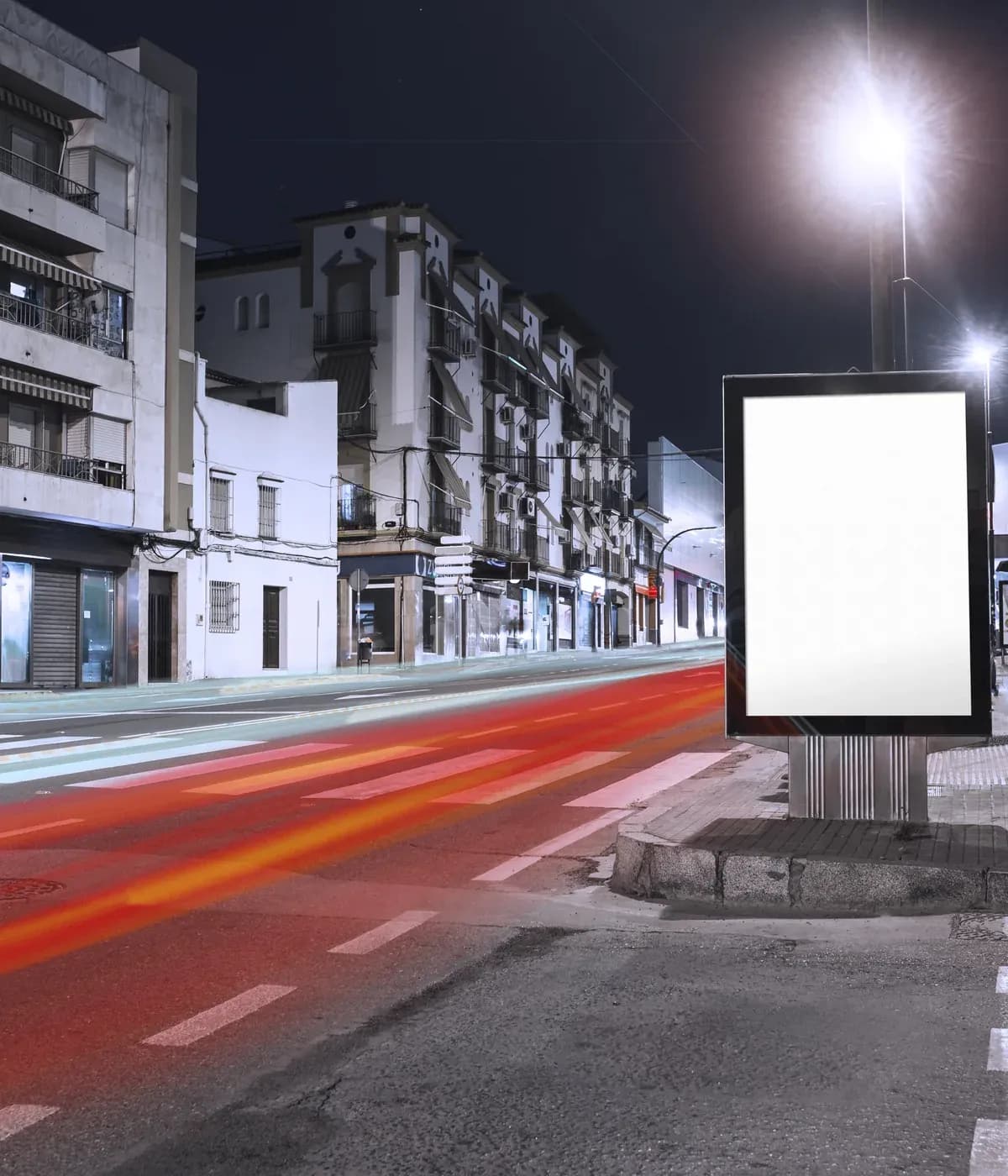 Painel publicitário na calçada com o movimento de carros à noite na cidade.