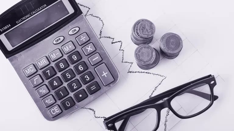 Calculadora, moedas e planilha sobre a mesa: o custo de contratar uma agência de marketing.
